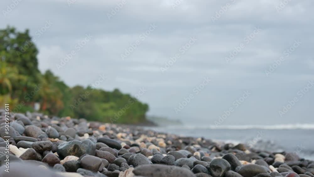 BALI, INDONESIA - JANUARY 30, 2018: Volcanic pebbled beach in the morning and blurred green trees and sea waves on background in Amed, Bali. 4K, Contains audio. Medium shot BALI, INDONESIA - JANUARY 30, 2018: Volcanic pebbled beach in the morning and blurred green trees and sea waves on background in Amed, Bali. 4K, Contains audio. Medium shot
