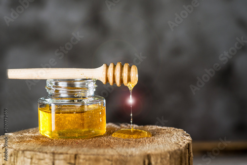 Honey jar and dripper on tree stump. grey background.