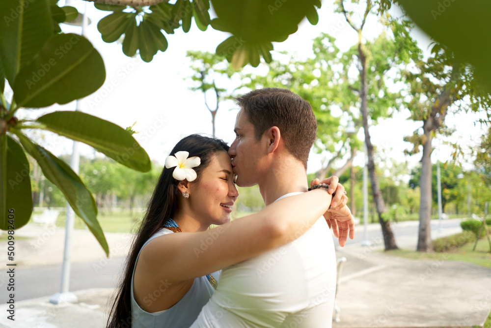 Fototapeta premium Man kissing a woman with a flower in the hair in the middle of a park