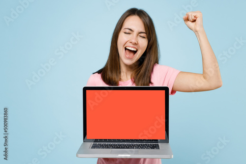 Young fun caucasian woman 20s wear pink t-shirt hold use work on laptop pc computer with blank screen workspace area do winner gesture isolated on pastel plain light blue background studio portrait.. © ViDi Studio