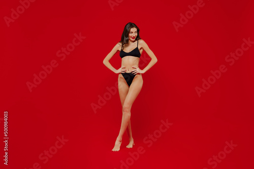 Full size young slender slim sexy hot woman 20s with perfect fit body wear black underwear hold hands on waist posing isolated on plain red background studio portrait. People female beauty concept