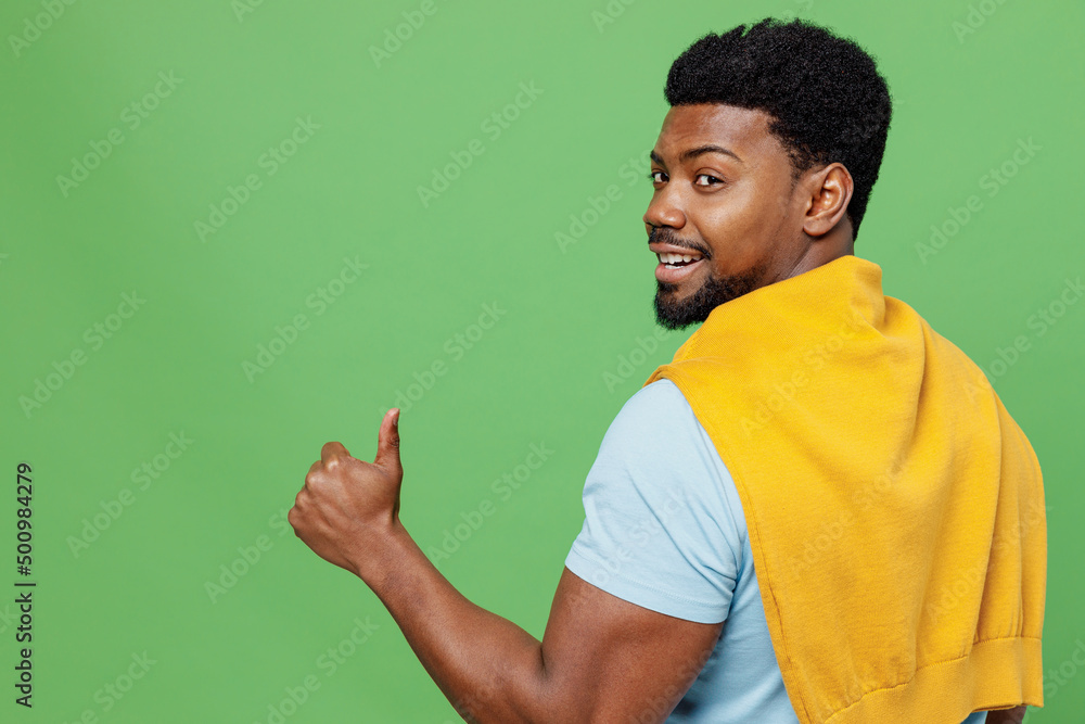 Back rear view young smiling happy man of African American ethnicity 20s wear blue t-shirt showing thumb up like gesture isolated on plain green background studio portrait. People lifestyle concept. Back rear view young smiling happy man of African American ethnicity 20s wear blue t-shirt showing thumb up like gesture isolated on plain green background studio portrait. People lifestyle concept.