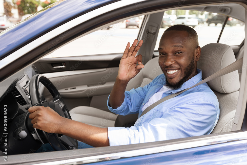 Happy black man sitting in car showing okay gesture
