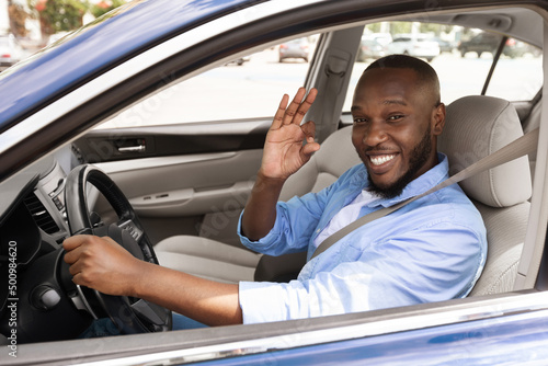 Happy black man sitting in car showing okay gesture © Prostock-studio