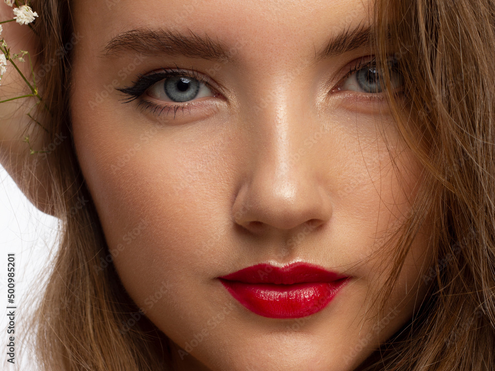 Close up portrait of a face with beautiful skin and evening makeup, eyeliner and long eyelashes, puffy red lips and white flowers. Fashion photography. Cosmetology and spa. Freshness of spring Close up portrait of a face with beautiful skin and evening makeup, eyeliner and long eyelashes, puffy red lips and white flowers. Fashion photography. Cosmetology and spa. Freshness of spring