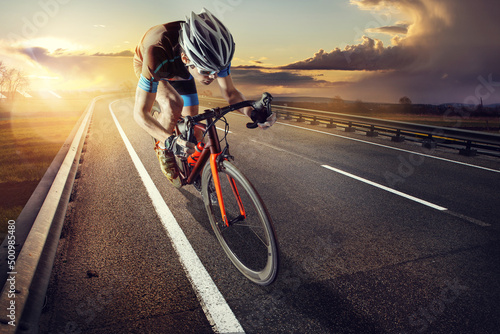 The cyclist rides on his bike at sunset. Dramatic background. photo