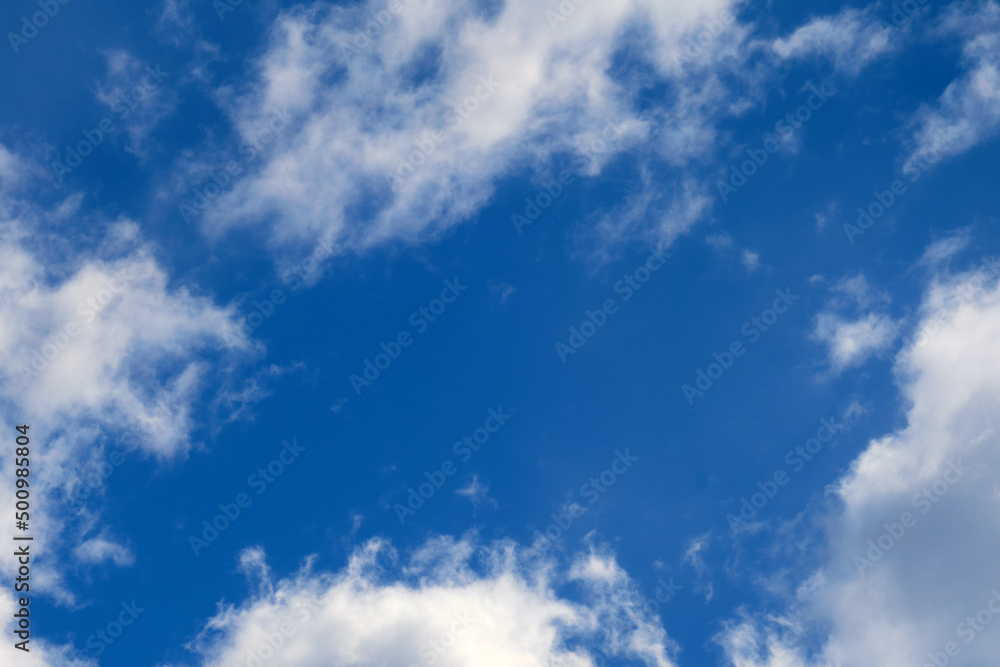 Blue sky background with soft fluffy white clouds, copy space in the center