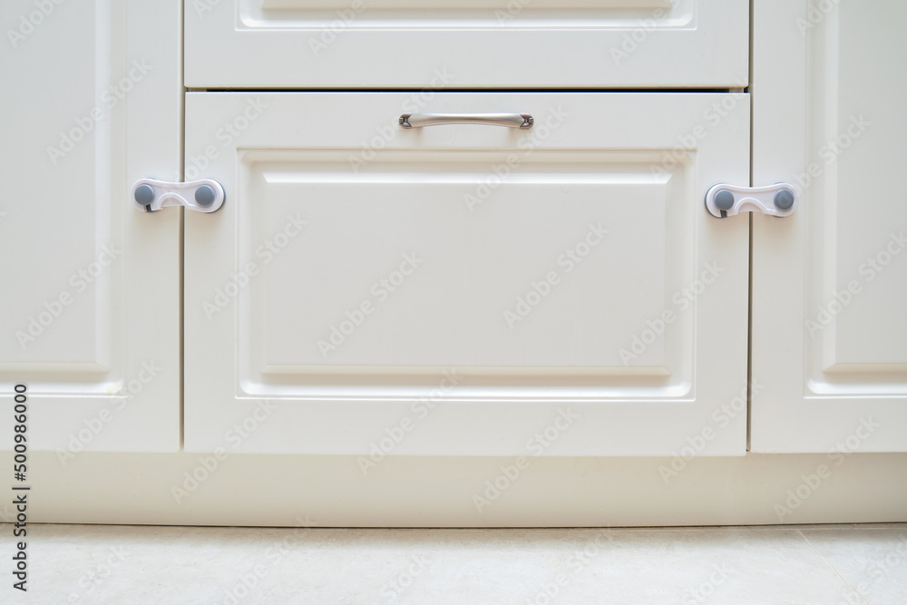 Doors of white kitchen cabinets blocked from children. Lock furniture drawers from toddler baby Doors of white kitchen cabinets blocked from children. Lock furniture drawers from toddler baby