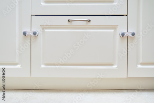 Doors of white kitchen cabinets blocked from children. Lock furniture drawers from toddler baby