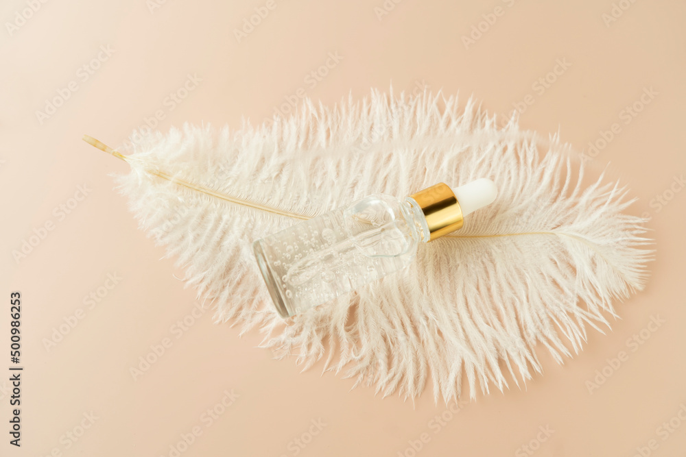 A white feather and a face serum or natural oil lying on a beige background A white feather and a face serum or natural oil lying on a beige background
