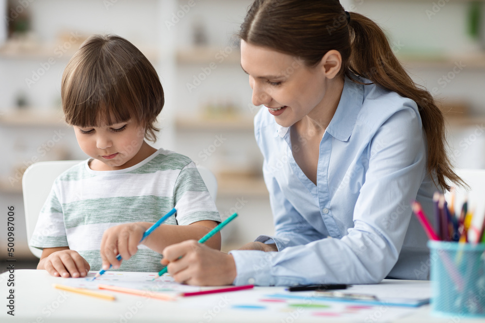 Happy woman teacher exercising with little student, happy boy coloring pictures, enjoying development classes Happy woman teacher exercising with little student, happy boy coloring pictures, enjoying development classes