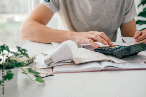 A man counts a bill on a calculator and a check for electricity on the table. Payment of utility services. Saving energy and money concept. photo