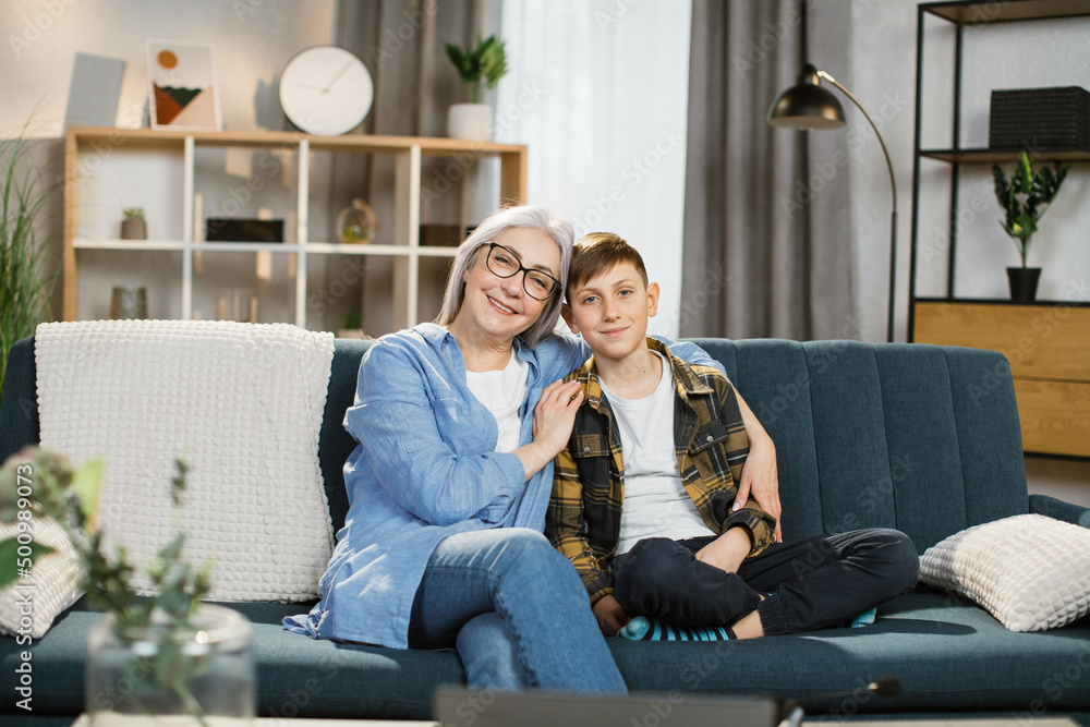 Portrait of a grandmother with her grandson, an old woman sits on the sofa, a boy hugs a great-grandmother, caring for a neighbor, family relationships, the older generation. Portrait of a grandmother with her grandson, an old woman sits on the sofa, a boy hugs a great-grandmother, caring for a neighbor, family relationships, the older generation.