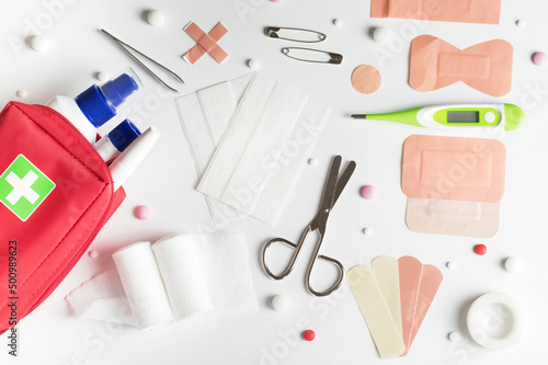 First aid kit accessories, scissors, band-aids, gauze pads, pills, thermometer among other items on white table