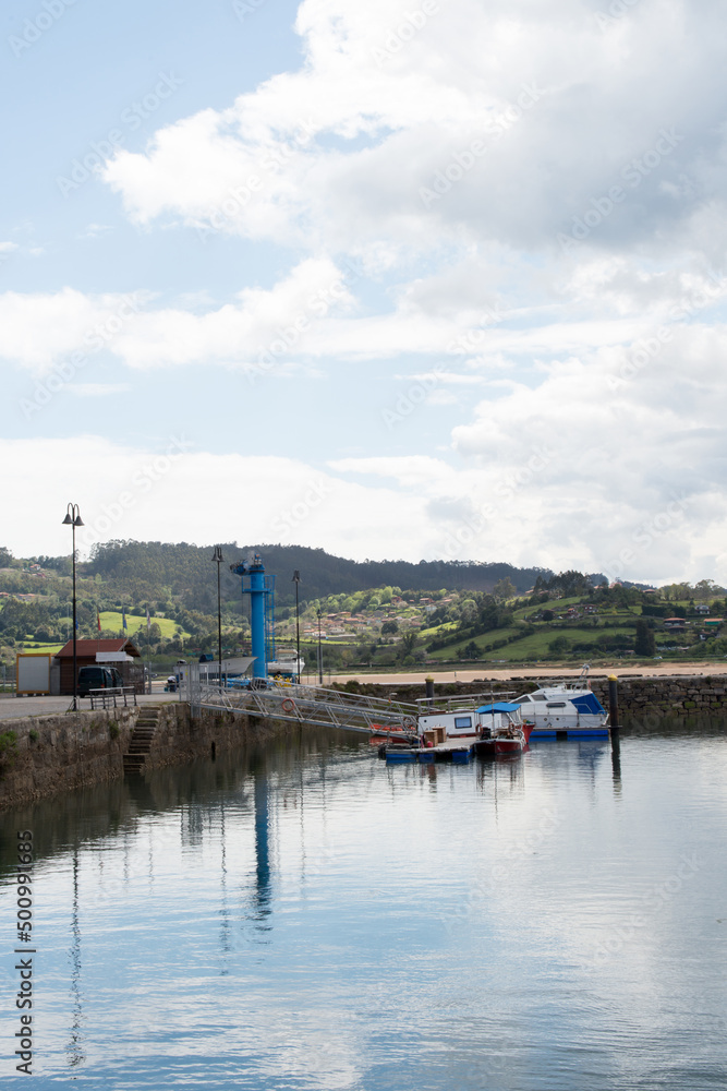 Fototapeta premium Vertical shot of asturian coast. Small harbour at El Puntal with two boats. Calm water, cloudy sky