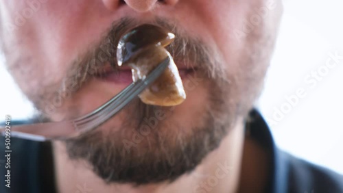 Bearded man eats pickled mushrooms. Close-up portrait of young guy puts boletus in mouth and chews with pleasure. Alternative protein source concept.
