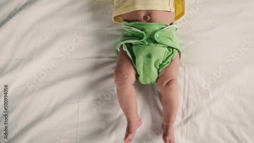 Unrecognizible crop shoot newborn baby in green reusable diaper on a white sheet. Modern eco friendly cloth nappy for infant child hygiene. Sustainable lifestyle, zero waste concept. photo