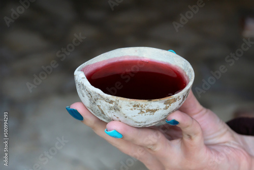 A woman's hand holds a bowl with a red Mayan ritual drink. Ancient shell with hibiscus tea. photo