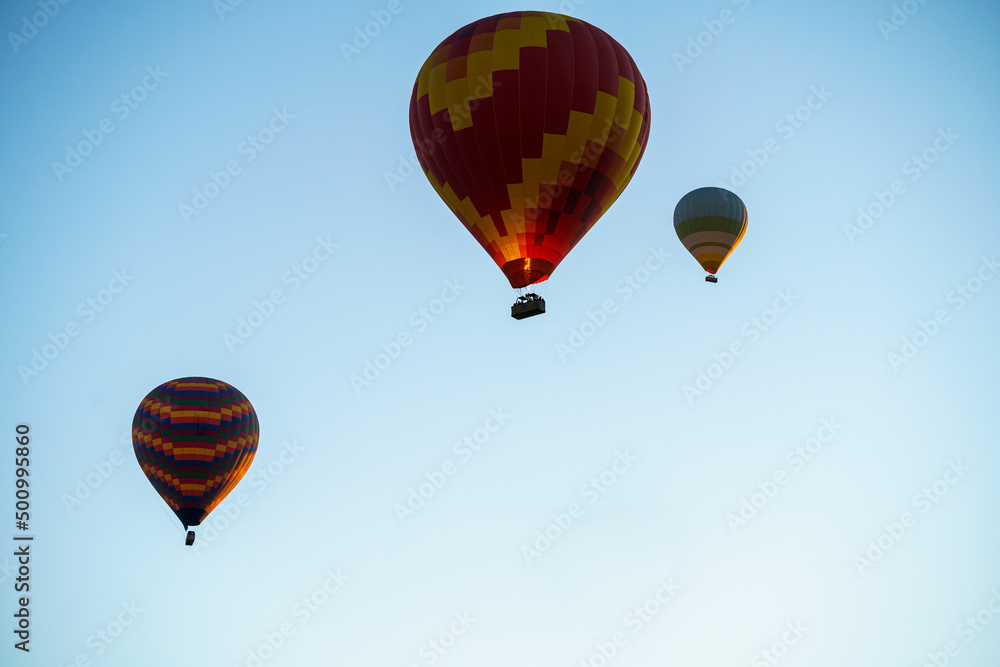 Fototapeta premium Balloons burning fuel as they fly over the city of Goreme with sightseeing tourists during a sunny summer day