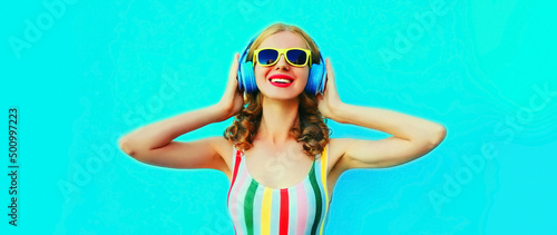 Portrait of modern happy smiling young woman listening to music in headphones on blue background