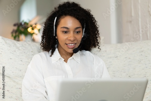 Smiling African American woman in headset using laptop, talking, working customer support service operator at home