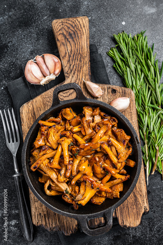 French roasted chanterelle mushrooms with onions and thyme in a pan. Black background. Top view
