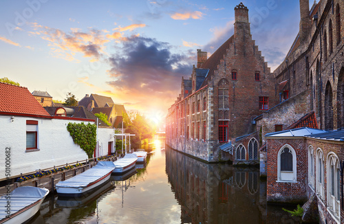 Bruges, Belgium. Medieval ancient houses made of old bricks at water channel with boats in old town. Summer sunset with sunshine. Picturesque landscape.