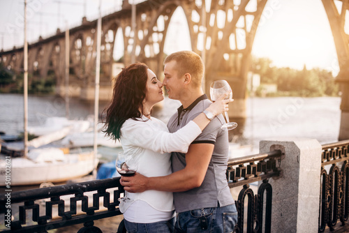Fotografia Loving couple hugging and drink wine while standing on embankment near boats in