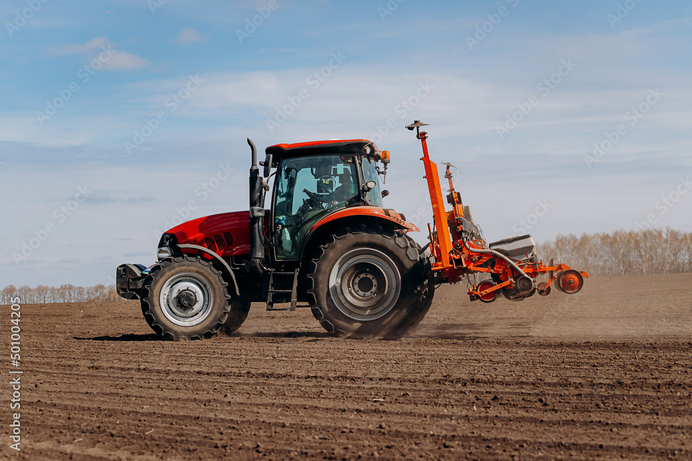 Obraz premium Spring sowing season. Farmer with a tractor sows corn seeds on his field. Planting corn with trailed planter. Farming seeding. The concept of agriculture and agricultural machinery.