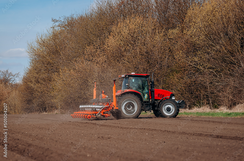 Spring sowing season. Farmer with a tractor sows corn seeds on his field. Planting corn with trailed planter. Farming seeding. The concept of agriculture and agricultural machinery. Spring sowing season. Farmer with a tractor sows corn seeds on his field. Planting corn with trailed planter. Farming seeding. The concept of agriculture and agricultural machinery.