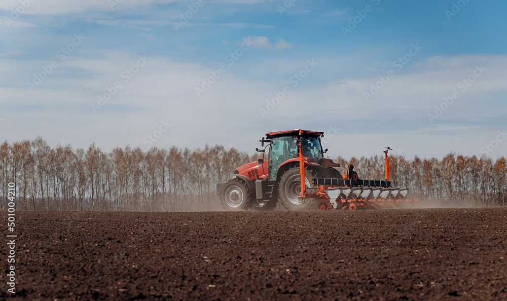 Obraz premium Spring sowing season. Farmer with a tractor sows corn seeds on his field. Planting corn with trailed planter. Farming seeding. The concept of agriculture and agricultural machinery.