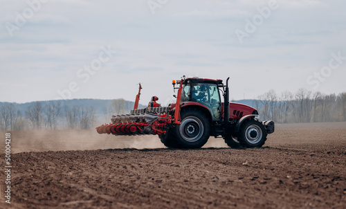 Spring sowing season. Farmer with a tractor sows corn seeds on his field. Planting corn with trailed planter. Farming seeding. The concept of agriculture and agricultural machinery.