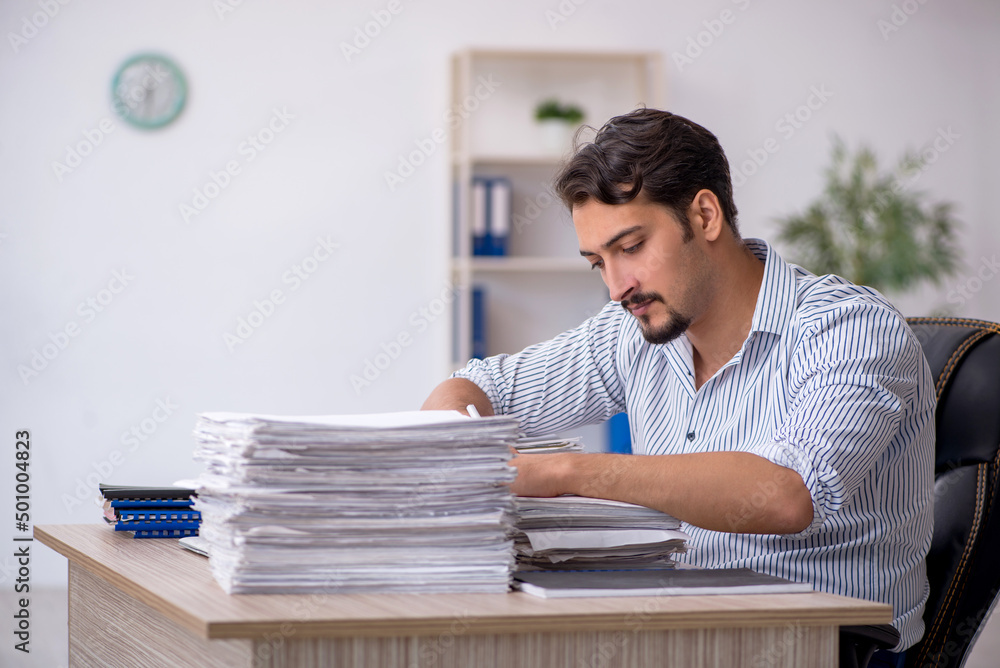 Young male employee unhappy with excessive work in the office Young male employee unhappy with excessive work in the office