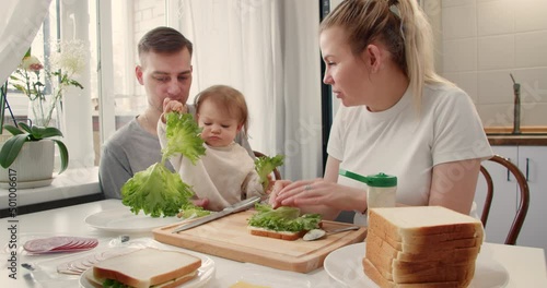 Mom making a sandwich with salad, ham and cheese for husbend and little doughter. American cuisine. Fast food. Cooking photo