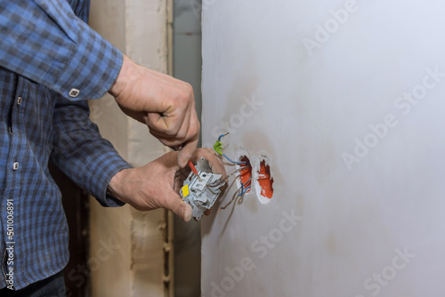 Hands of man electrician holding screwdriver working on the residential electric system installing power socket on wall at home repair