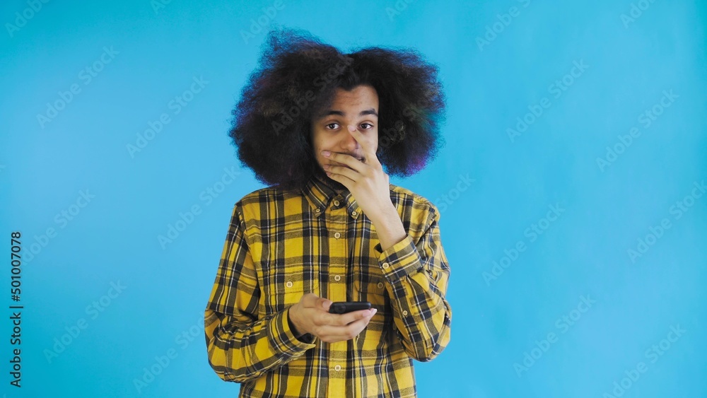 A young man with an African hairstyle on a blue background is talking into his phone. A young man with an African hairstyle on a blue background is talking into his phone.