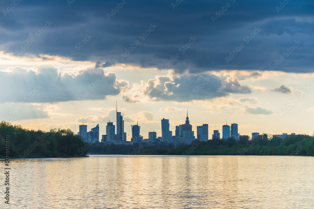 Sunny cloudy day big city of Warsaw skyline in spring, high skyscrapers over Wisla river surface. Downtown beautiful cityscape panorama lit with warm sunset light