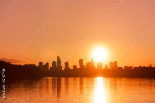 Big city skyline sunny evening in big city of Warsaw  Poland. High buildings skyscrapers on horizon over Wisla river surface. Sunset  downtown beautiful cityscape panorama lit with warm sun light