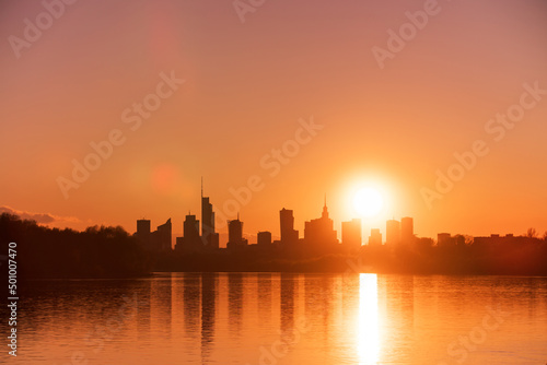 Big city skyline sunny evening in big city of Warsaw, Poland. High buildings skyscrapers on horizon over Wisla river surface. Sunset, downtown beautiful cityscape panorama lit with warm sun light