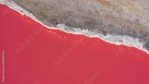 Flying over a pink salt lake. Salt production facilities saline evaporation pond fields in the salty lake. Dunaliella salina impart a red, pink water in mineral lake with dry cristallized salty coast. photo