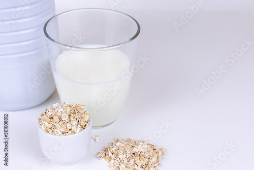 A glass of white oat milk and oatmeal flakes on white background. with copy space Vegetable milk