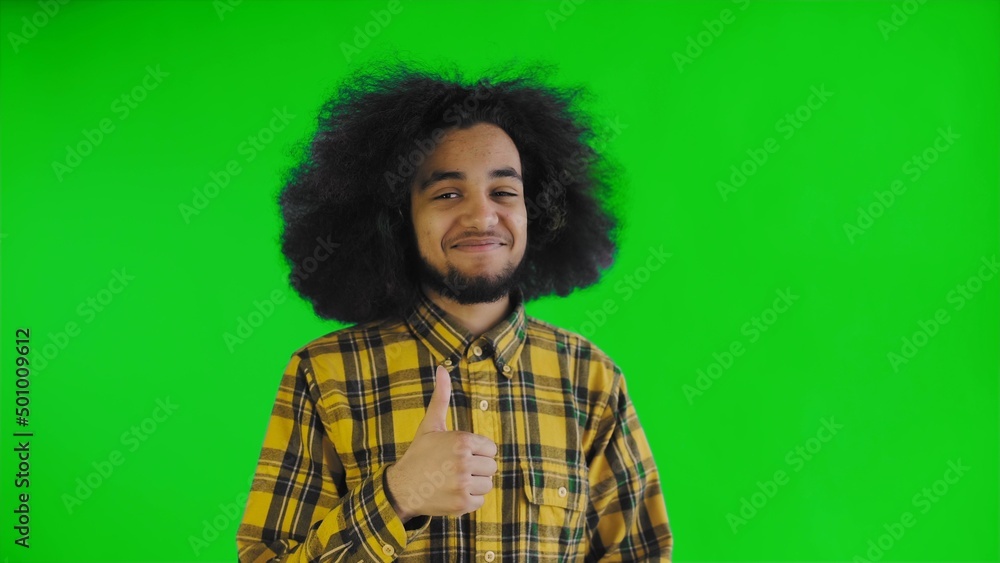 A happy African-American man looking into the camera, shows a like with his hand, stands isolated on a green background A happy African-American man looking into the camera, shows a like with his hand, stands isolated on a green background