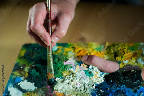Painter's hands taking a paint brush from his palette to paint an oil painting