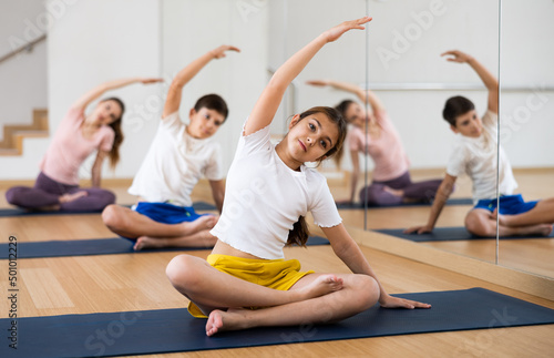 Girl doing exercises in lotus pose with her family in gym.