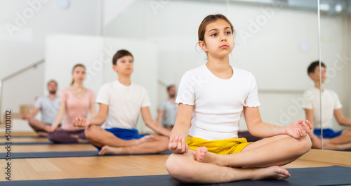 Young girl exercising lotus pose with her family during group yoga training.
