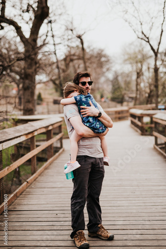 Father holds daughter outside on wooden walkway at zoo