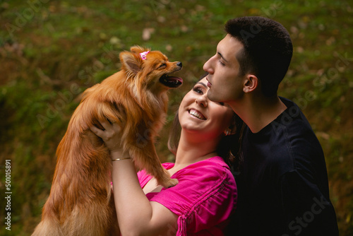 Woman holding a German spitz, while a man plays and makes her pet dog smile