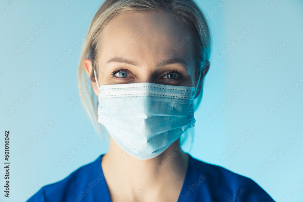 attractive young blonde European nurse smiling under the mask closeup studio shot blue background medical concept. High quality photo attractive young blonde European nurse smiling under the mask closeup studio shot blue background medical concept. High quality photo