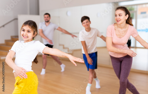 Happy sporty family of four enjoying active dance in modern studio. Focus on smiling brunette teenage girl..