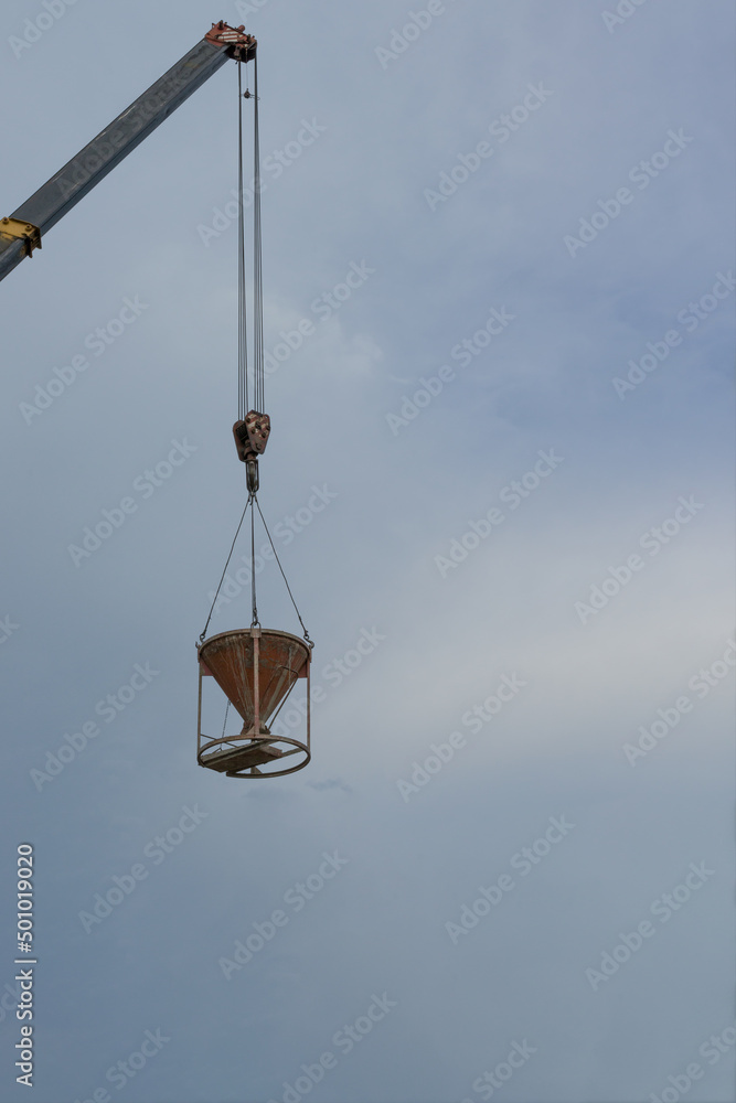 crane lifted a bucket of cement at a construction site against a blue sky